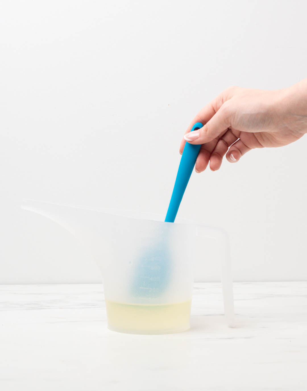 Hand stirring mixture with a spatula in pouring pitcher.